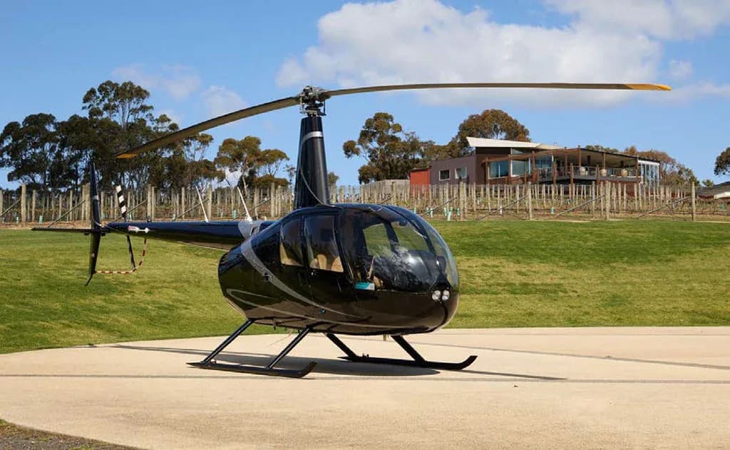 A black Robinson R44 helicopter with silver stripes on a paved area, viewed from the front.