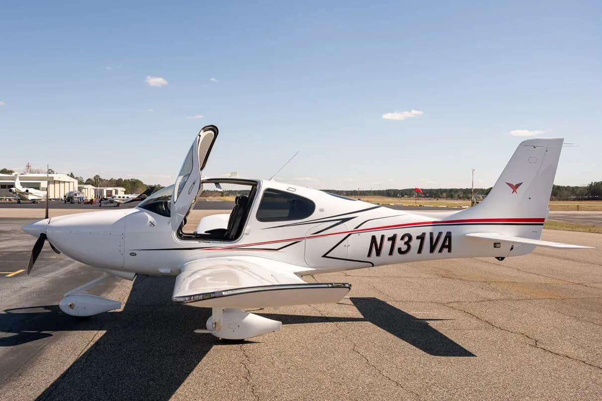 A white Cirrus SR22 aircraft with red and black accent stripes, tail number N131VA, parked on an airfield with the pilot's side door open.
