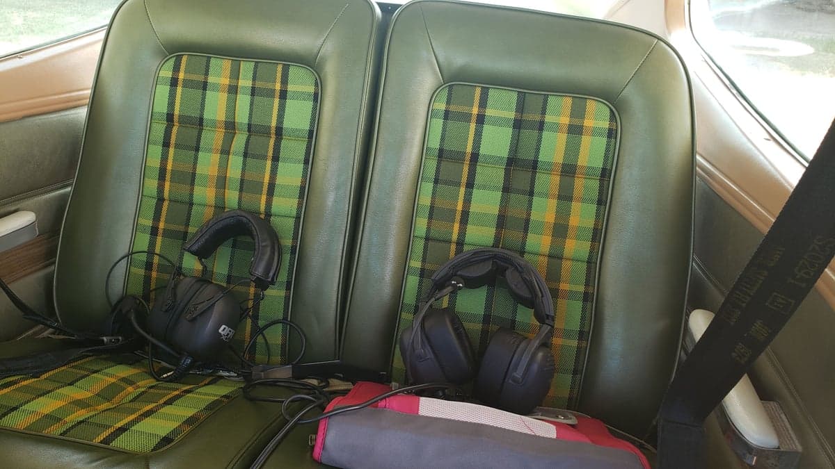 The interior of the aircraft features green plaid seats with headsets on them.
