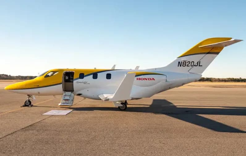 A HondaJet Elite with a yellow and white paint scheme, registration N820JL, parked on an asphalt tarmac with its main door open.