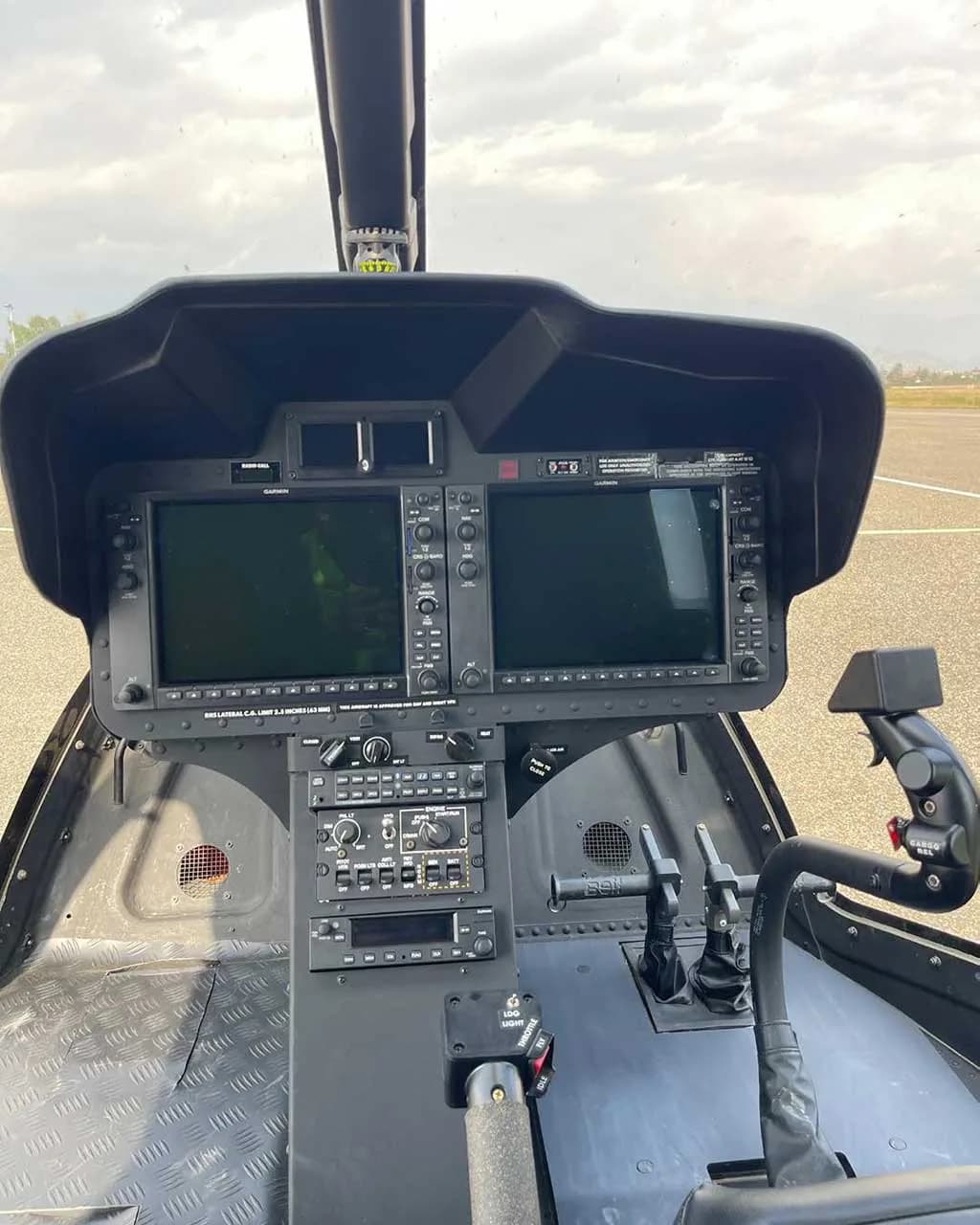 A detailed view of the helicopter's modern glass cockpit with two large display screens and various controls.