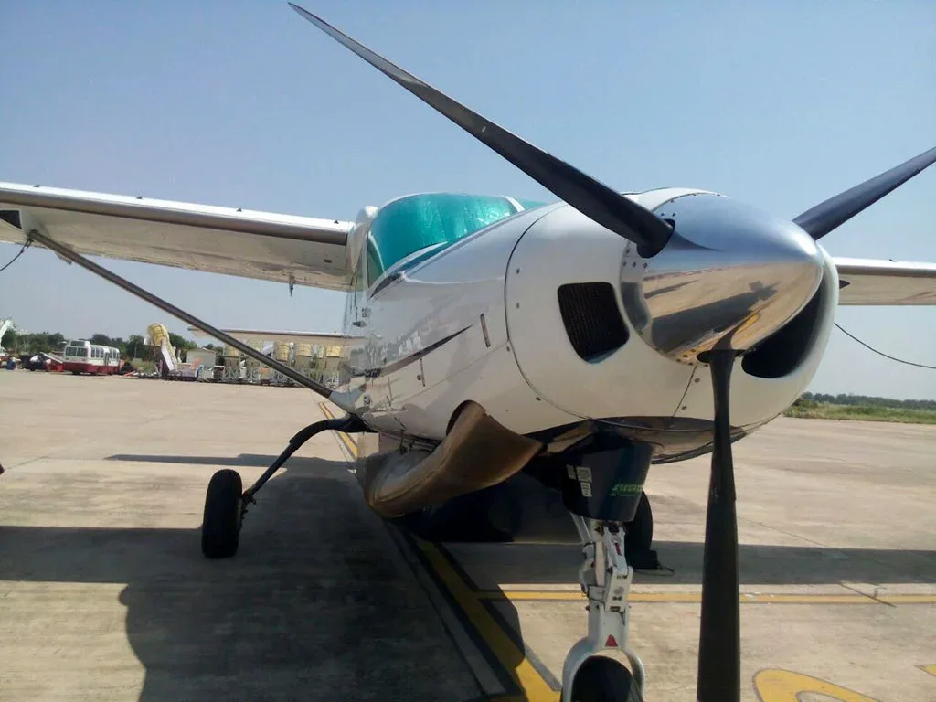 A front-quarter view of a white and blue single-engine turboprop aircraft with a shiny propeller spinner, parked on an airfield.