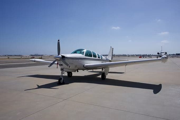 A Beechcraft Bonanza aircraft in a hangar with a white and gray paint scheme.