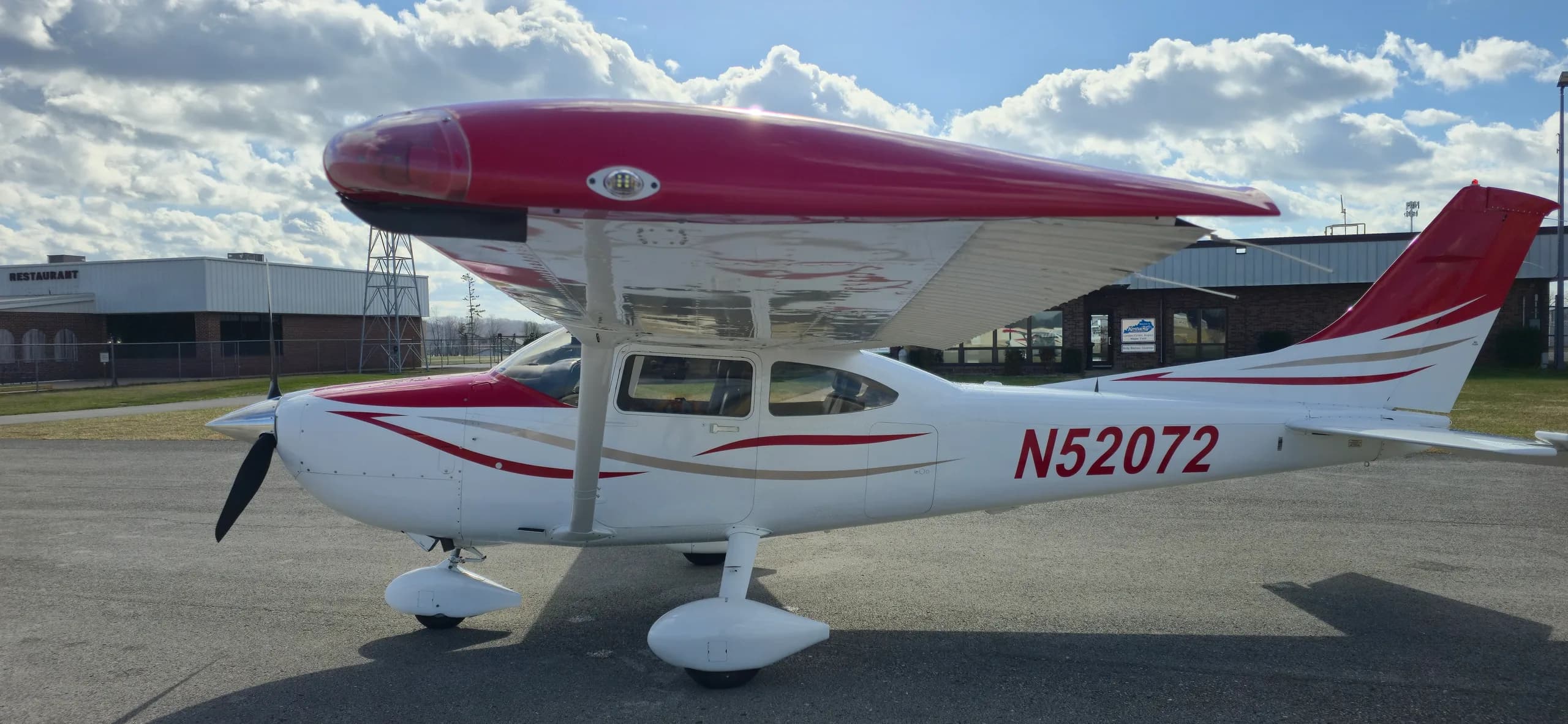 A white and red Cessna aircraft, registration N52072, parked on an asphalt tarmac under a partly cloudy sky.