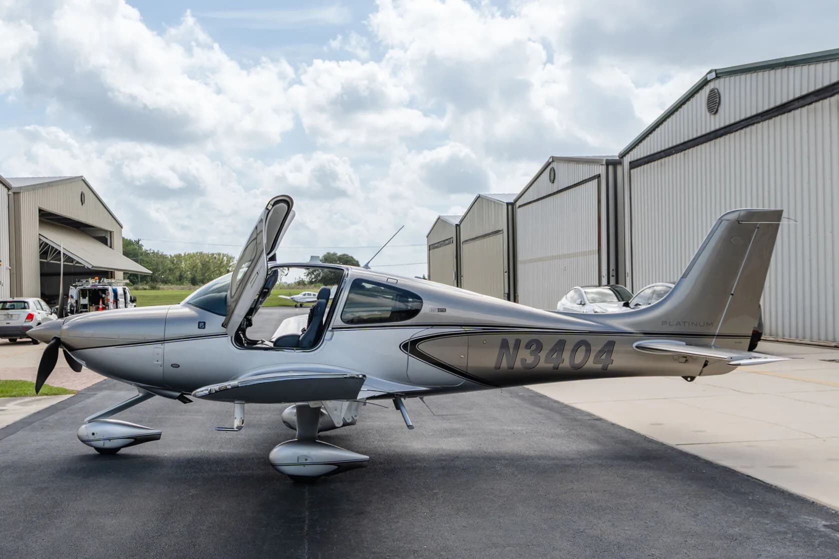 Side view of a silver Cirrus SR22T aircraft (N3404) with its gull-wing doors open, parked on an airport tarmac.