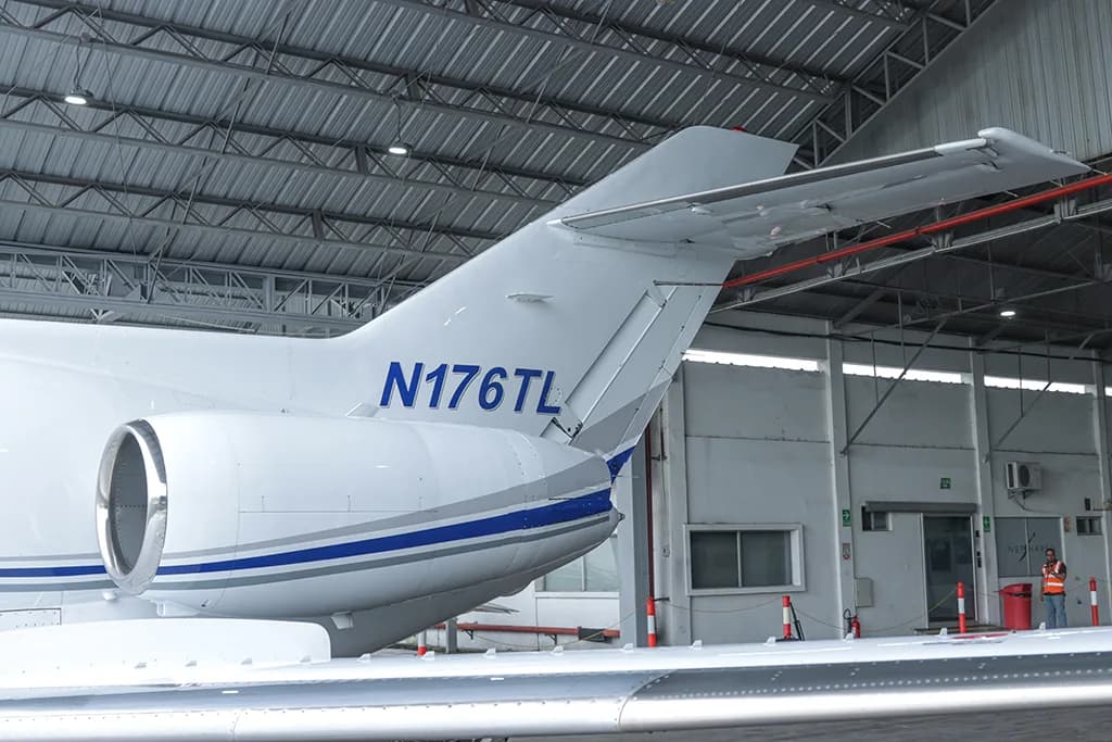 A rear-quarter view of the tail and engine of a white business jet with blue and grey stripes, registration N176TL, inside a hangar.
