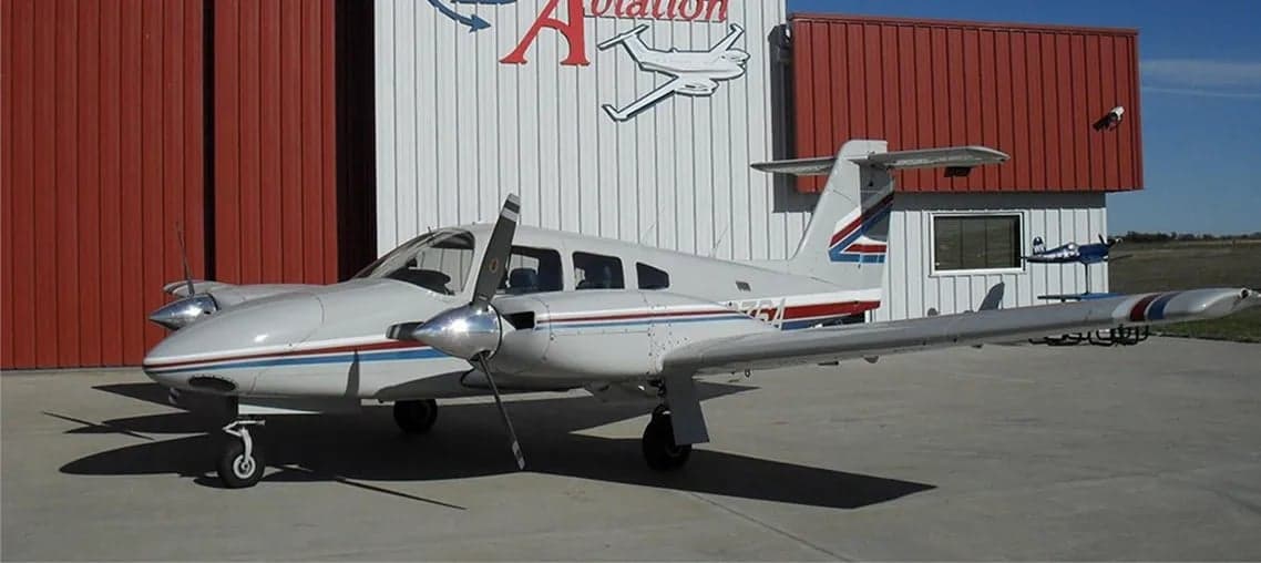 A Piper Twin Comanche aircraft parked outside a hangar.