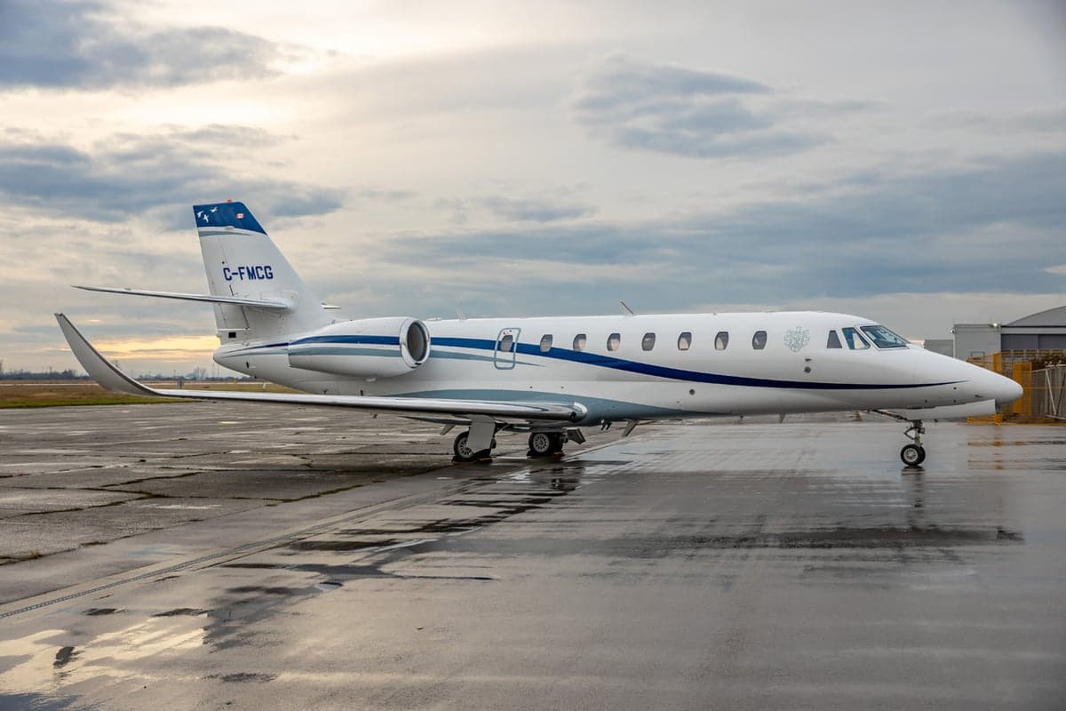 Front view of a white jet on a wet tarmac.