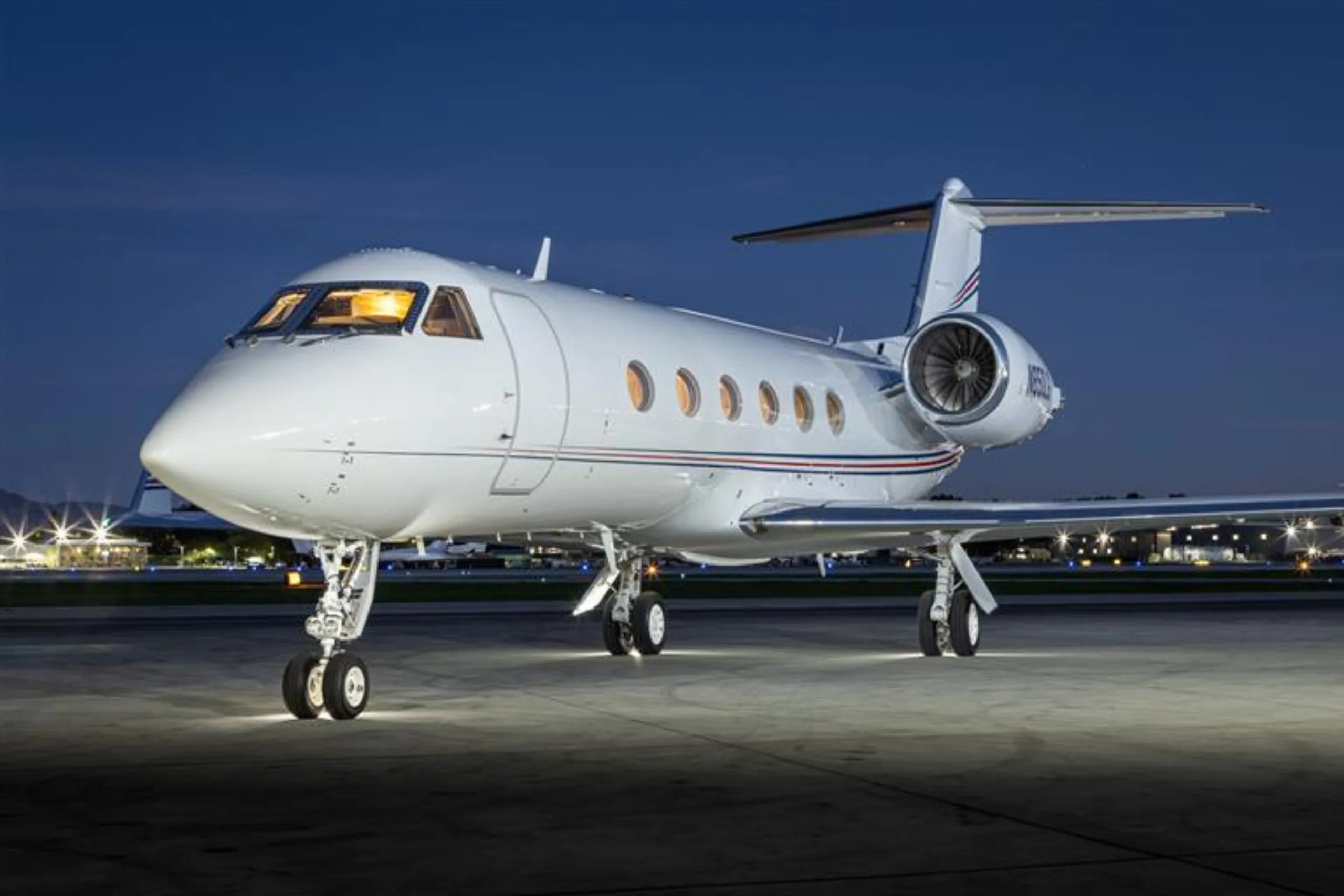 A white private jet parked on the tarmac at night.