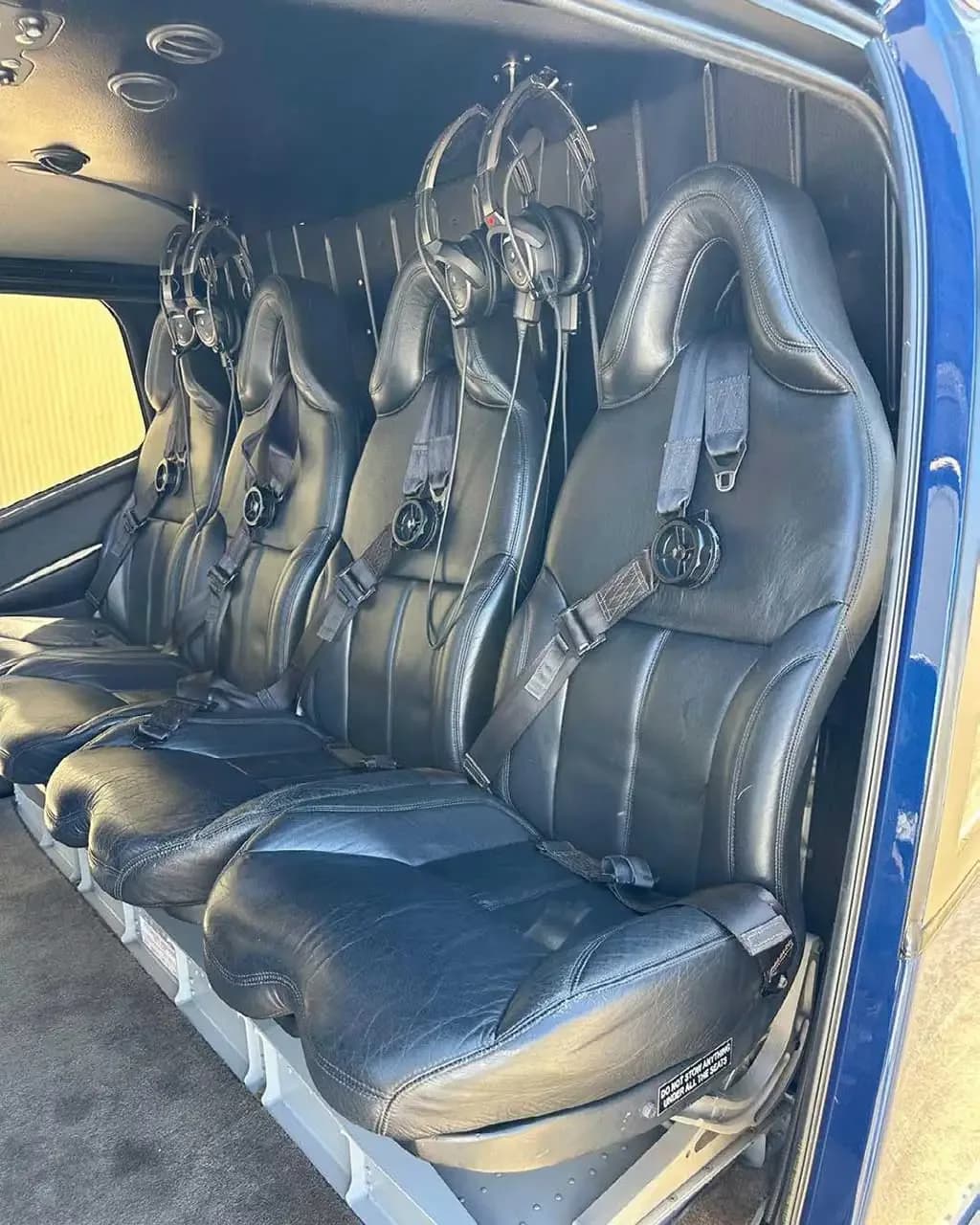 The interior cabin of a helicopter showing four black leather passenger seats with headsets.