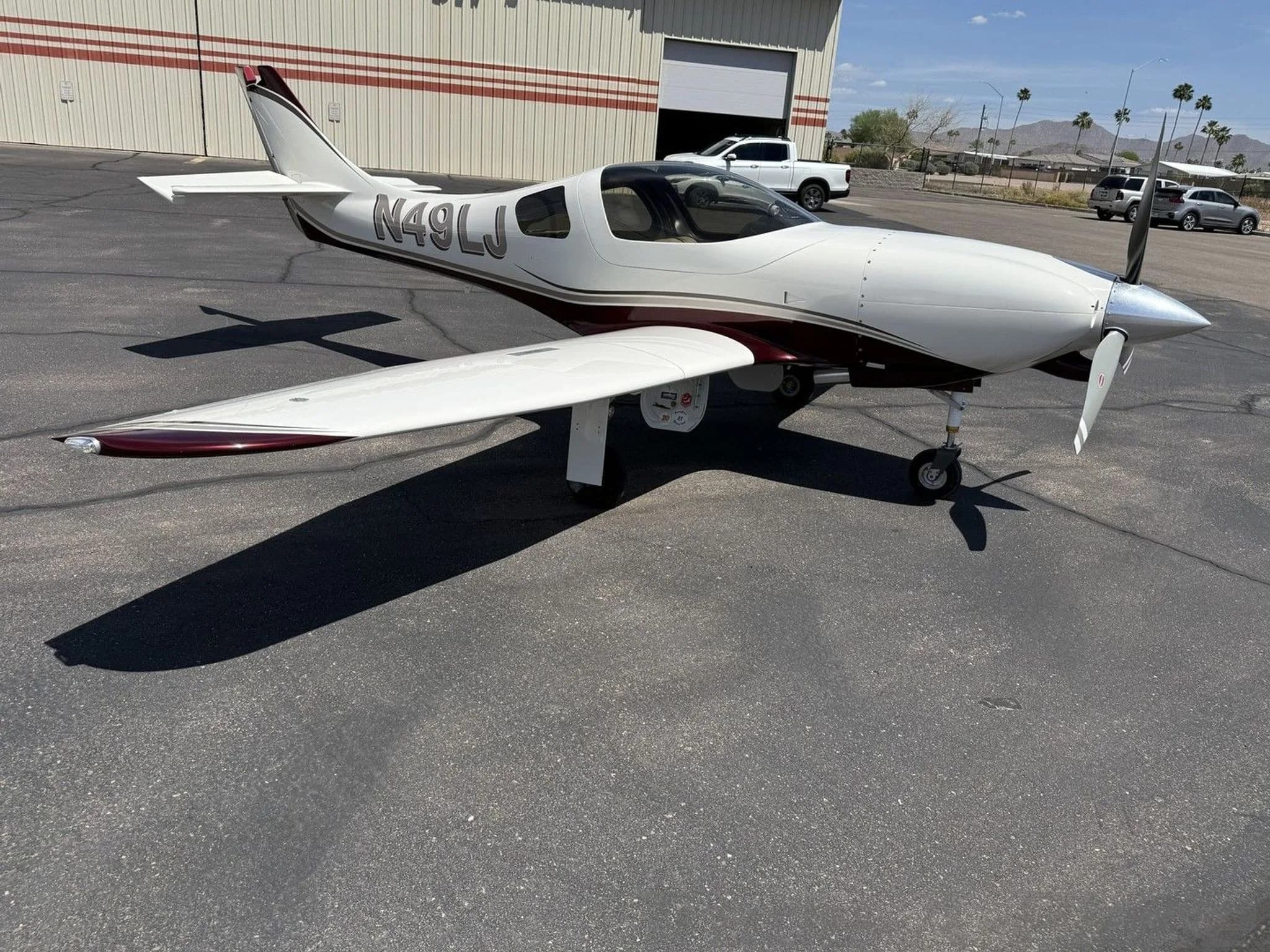 A white and maroon single-engine aircraft (N49LJ) parked on an asphalt apron in front of a hangar.