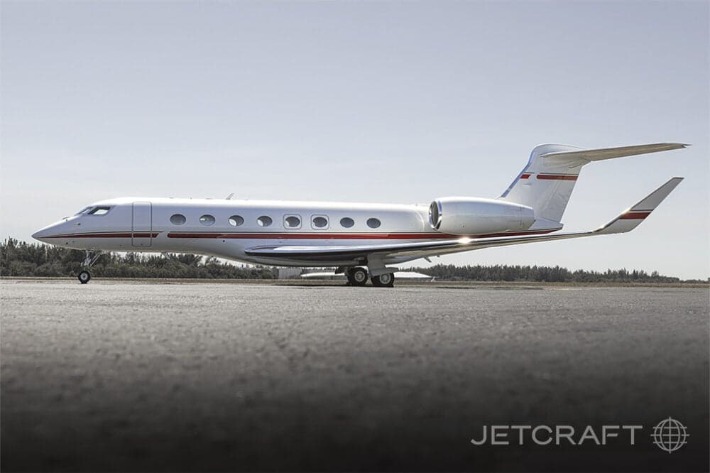 A white Gulfstream business jet with red and grey stripes parked on an asphalt runway under a clear sky.