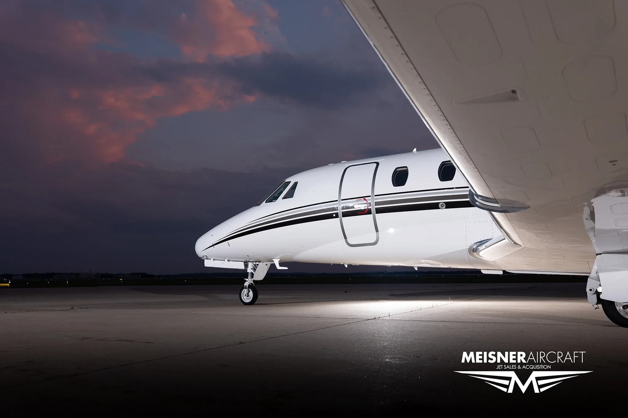 A close-up view of the front fuselage and wing of a white Citation Excel business jet on a tarmac at dusk.