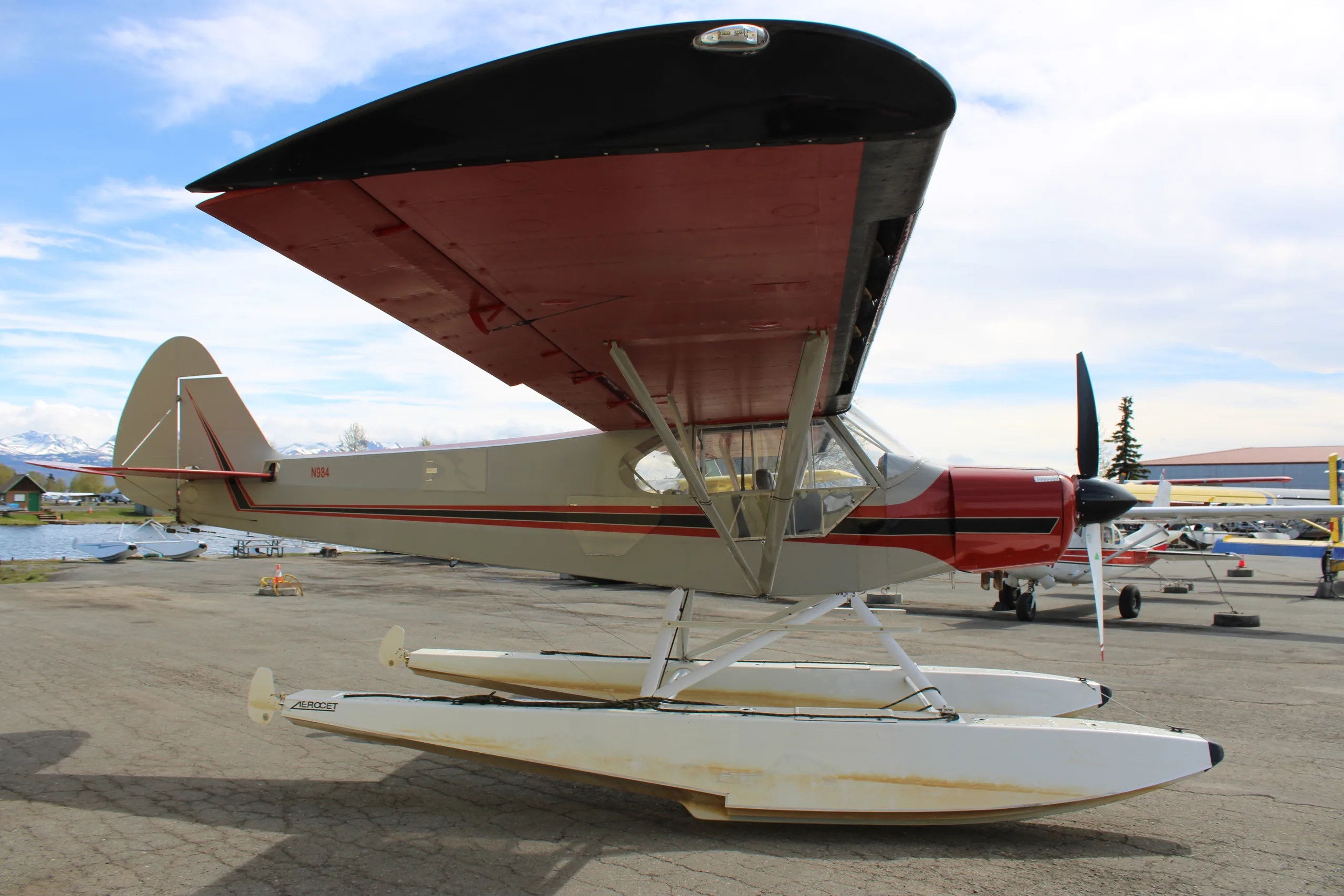 A red and silver float plane is parked on the tarmac, side view.