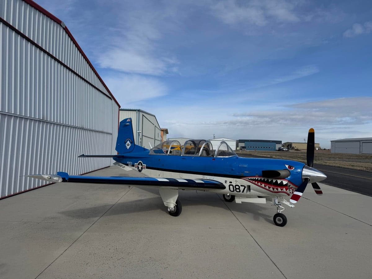 A blue and white SIAI-Marchetti SF.260 is parked on the tarmac with a shark mouth paint scheme.