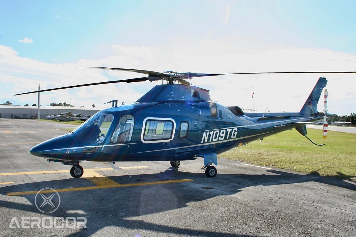 Side view of a blue AgustaWestland AW109 helicopter (N109TG) parked on an airfield.