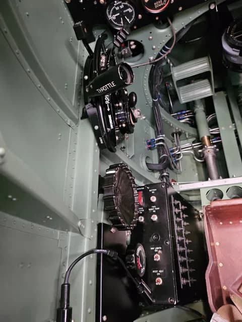 A detailed view of the throttle quadrant and control panels on the left side of a Supermarine Spitfire cockpit.