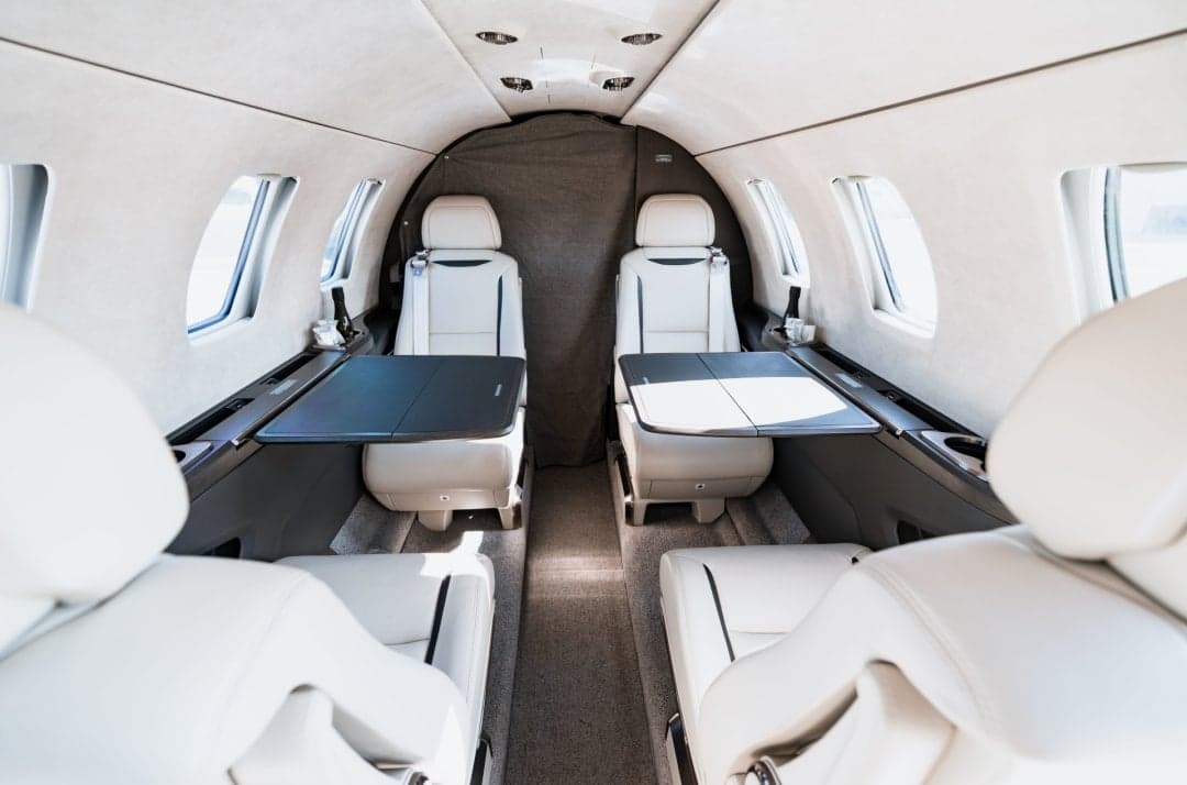 View of the interior of the aircraft cabin with white leather seats and tables.