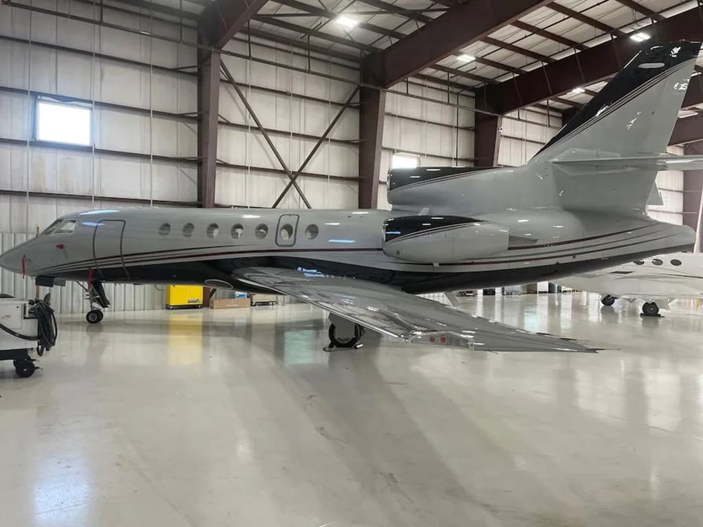 A grey and black Dassault Falcon 900 business jet is parked inside a hangar.