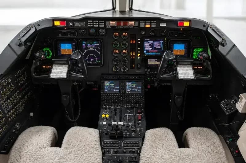 The aircraft cockpit features a complex array of digital displays, analog gauges, and controls, with two pilot seats.