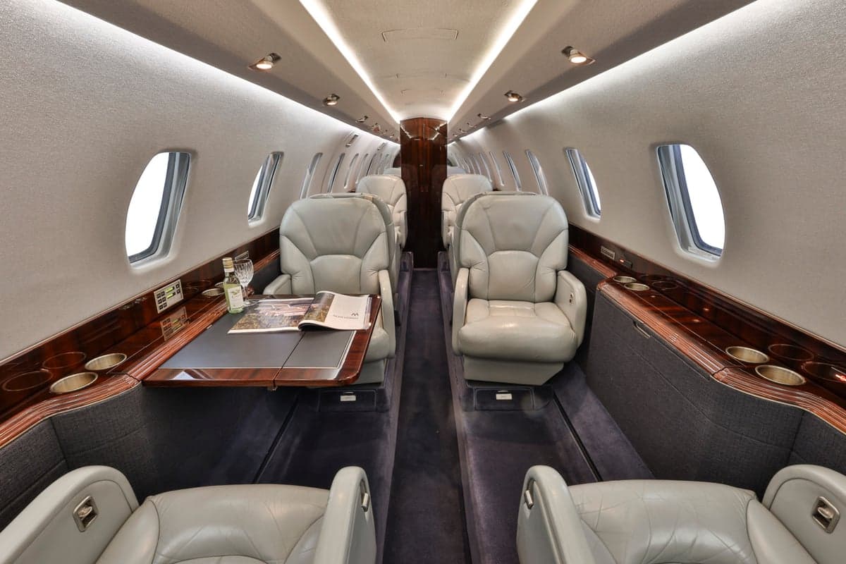 The interior of a Citation CJ3 aircraft, showing the cabin seats and a table with a magazine and wine bottle.