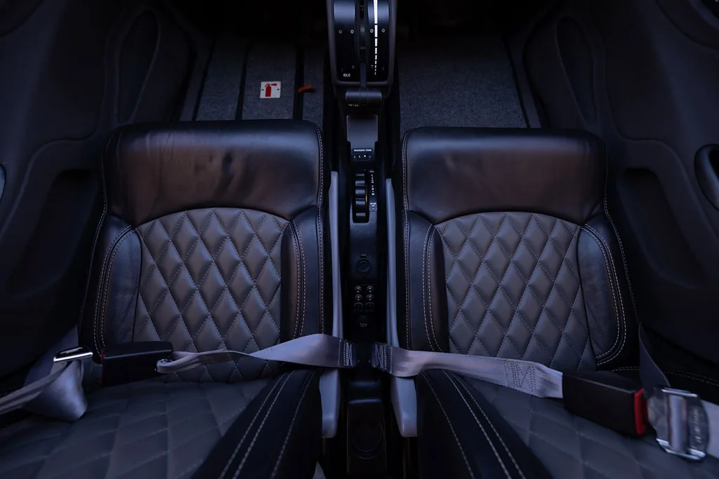 An overhead view of two black leather aircraft seats with quilted stitching and the central console.