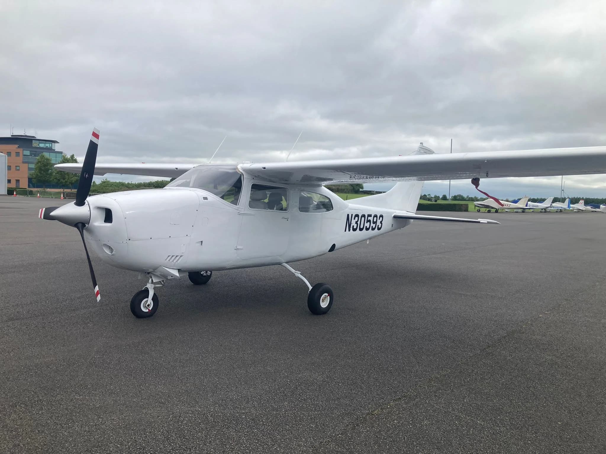 A white Cessna 172 aircraft N30593 parked on an airfield with several other planes in the background.