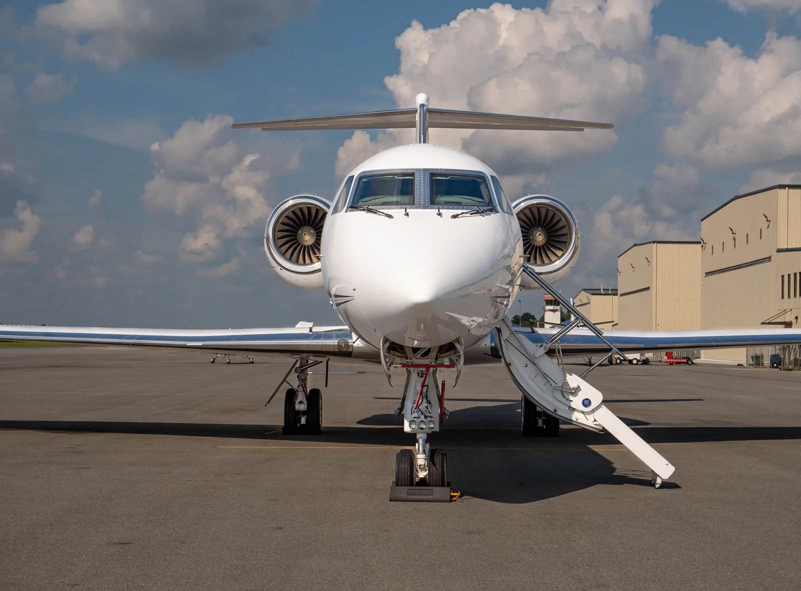 Front view of a white jet aircraft on the tarmac with the airstair door open.