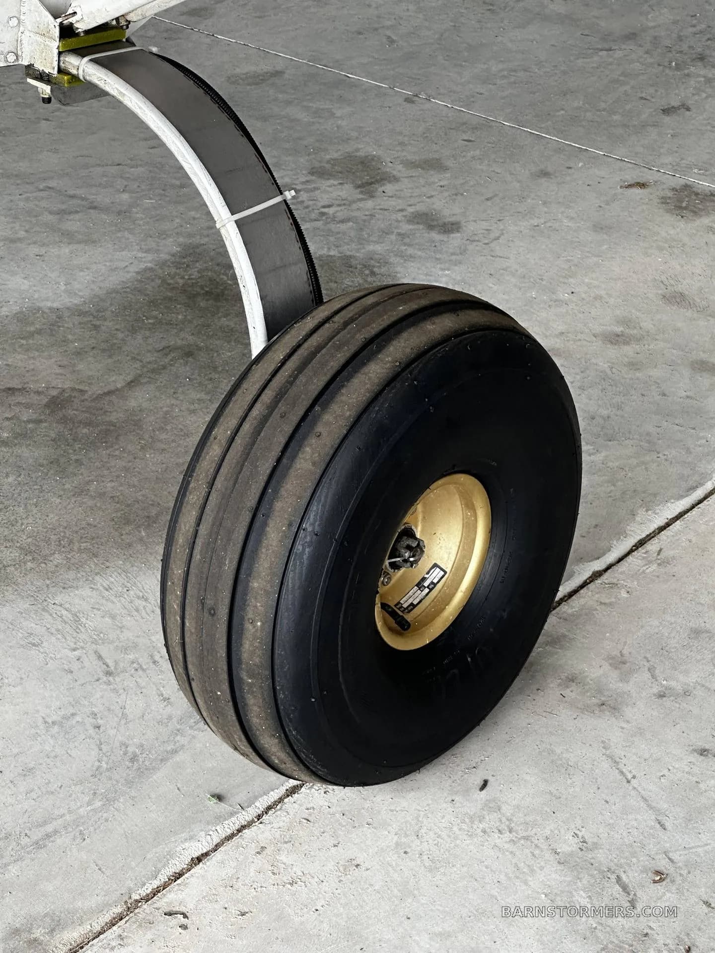 A close-up of a large, black aircraft tire with a gold hub on a concrete surface.