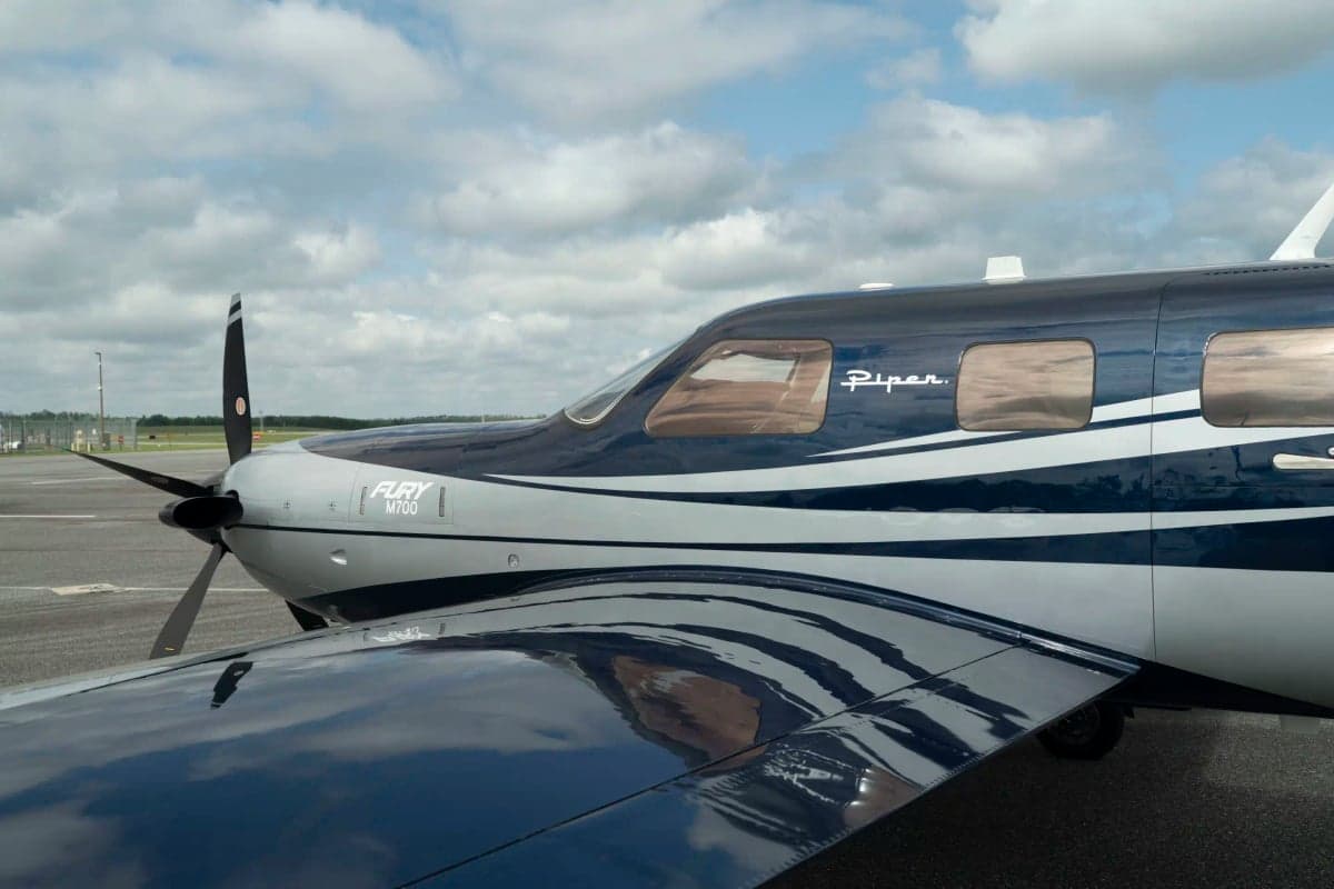 A close-up view of the nose and left wing of the Piper M700 Fury aircraft, highlighting the propeller and 'Fury M700' designation.