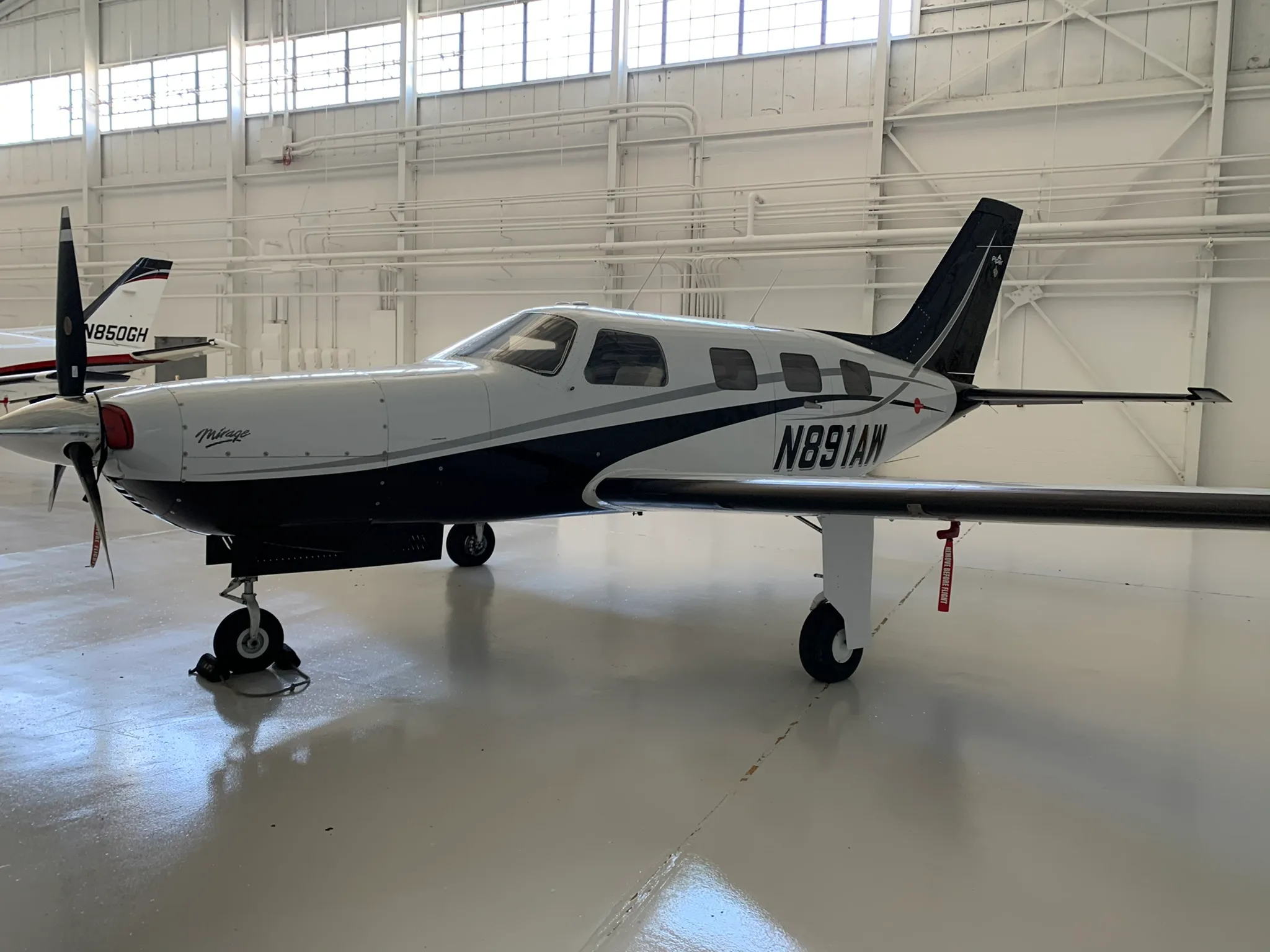 A white and black Piper Mirage aircraft (N891AW) is parked in a brightly lit hangar, viewed from the side.