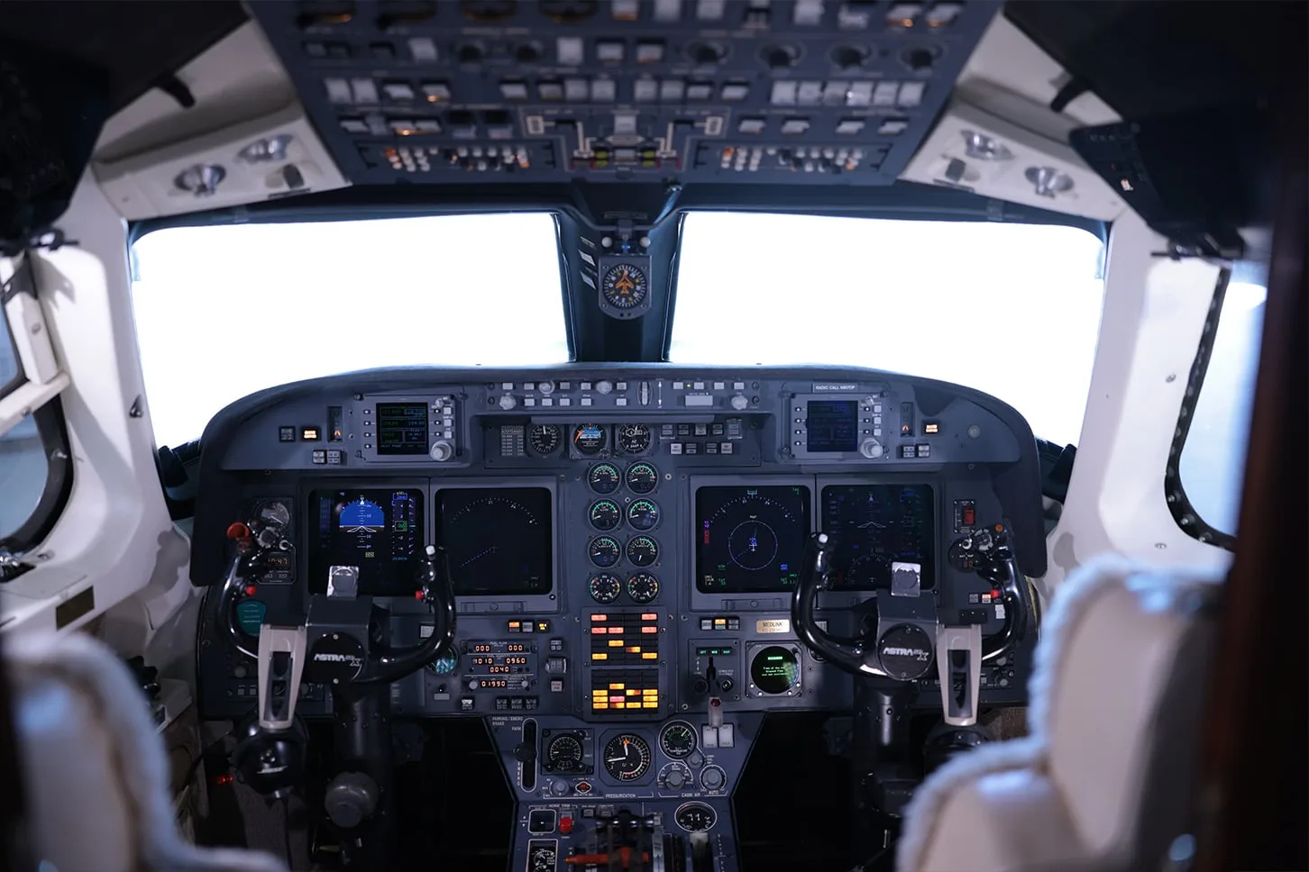 The detailed instrument panel and controls of a private jet cockpit, with screens and numerous buttons.
