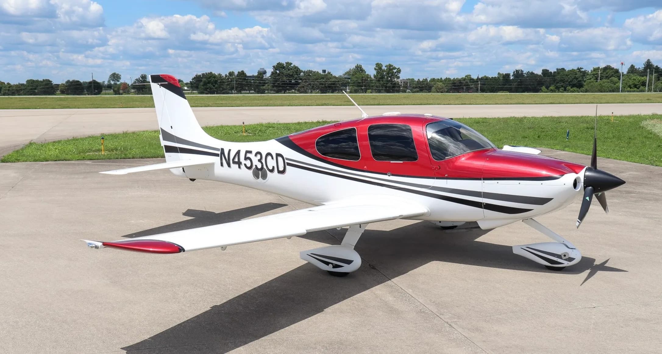 A three-quarter side view of a white and red single-engine aircraft with tail number N453CD on an airfield.