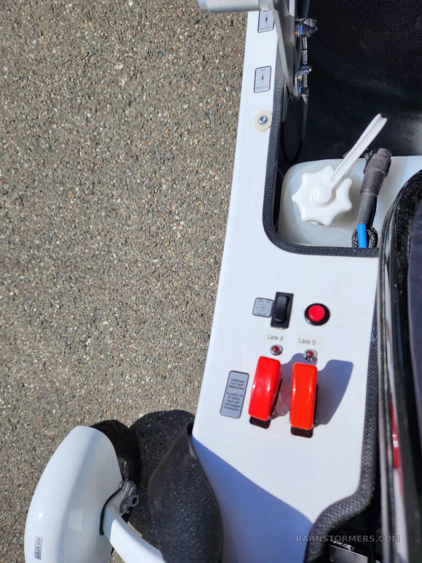 A close-up view of the white control panel of a gyrocopter, showing switches, buttons, and a fuel cap.