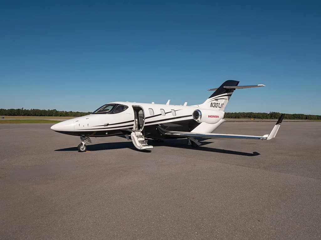 A white and black HondaJet N301JT is parked on an asphalt tarmac with its main door open on a clear day.