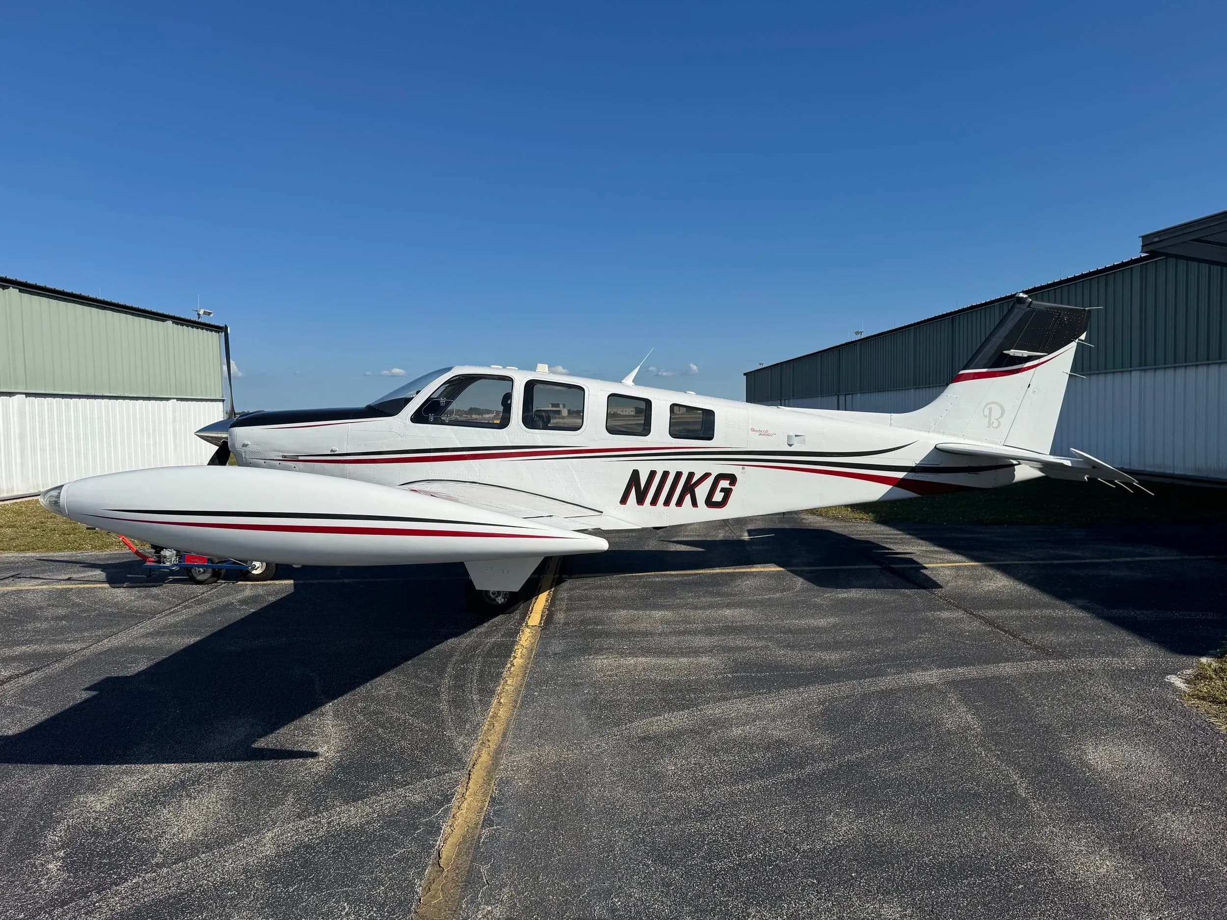 A Beechcraft Bonanza with a white and black paint scheme is parked on the tarmac.