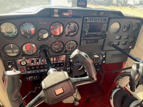 The cockpit of a Cessna aircraft showing the instrument panel, yokes, and avionics.
