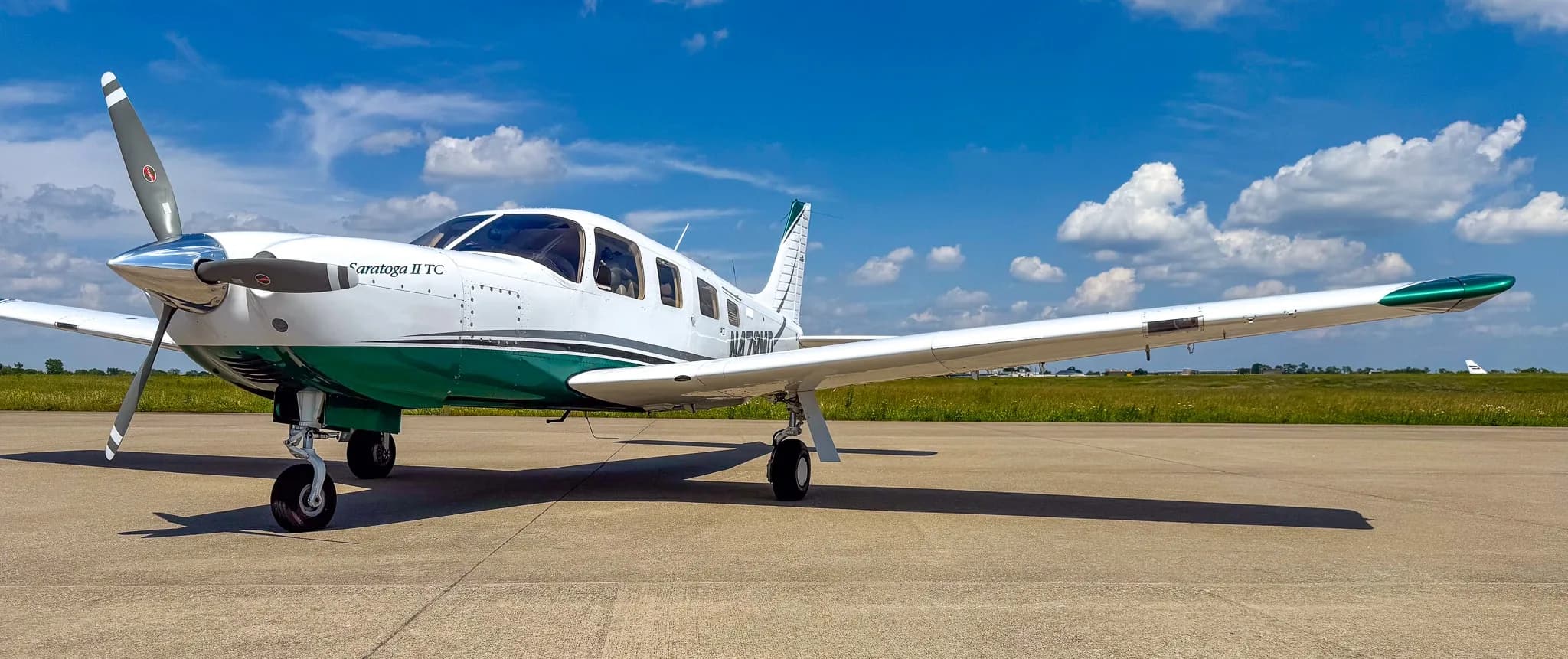 A white and green Piper Saratoga II TC aircraft (N478MD) with its propeller visible, parked on an airfield under a blue sky.