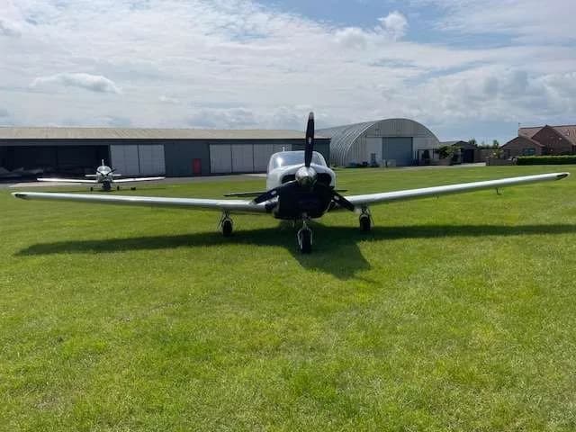 Front view of a white and blue single-engine aircraft with a propeller, parked on a grassy airfield.