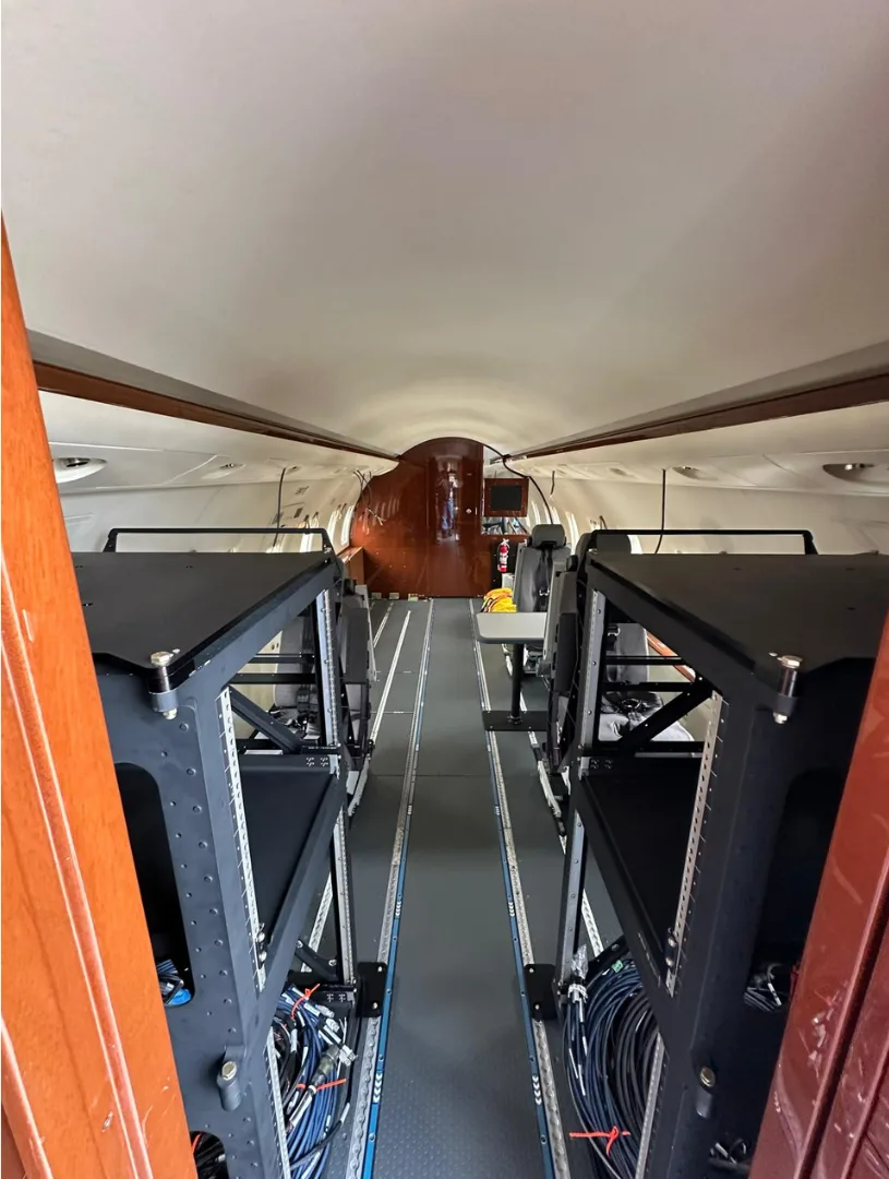 The aircraft's interior cabin, configured with equipment racks on both sides, looking towards the front.