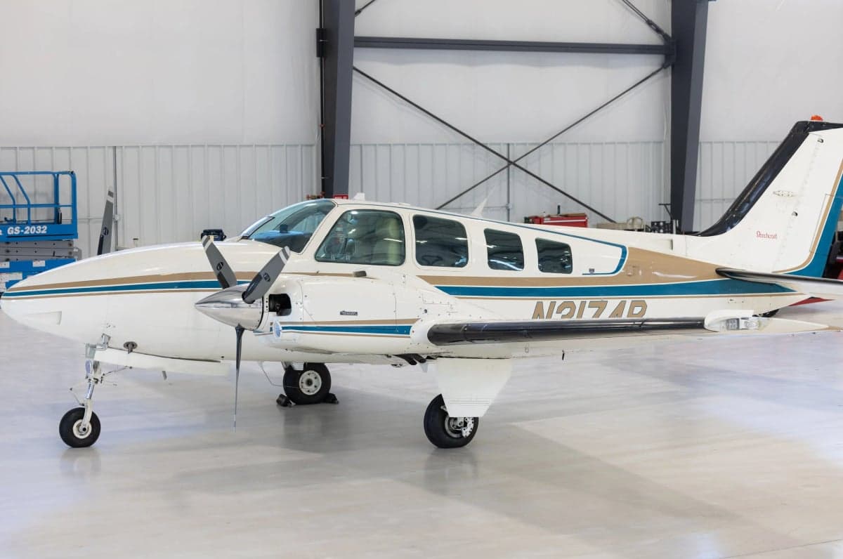 A Beechcraft Bonanza with a white and tan paint scheme parked in a hangar.