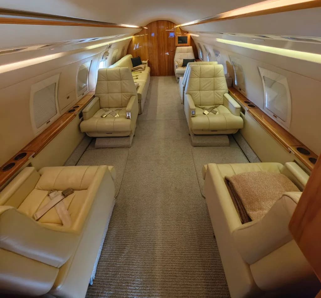 The luxurious cabin interior of the business jet, featuring light beige leather seats and wood paneling.