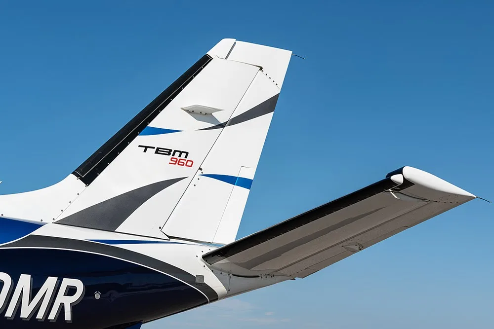 A close-up view of the tail and horizontal stabilizer of the TBM 960 aircraft with blue and white paint.