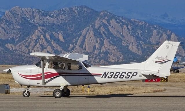 Cessna 172 Skyhawk with red stripes and tail number N386SP parked on the tarmac with mountains in the background.