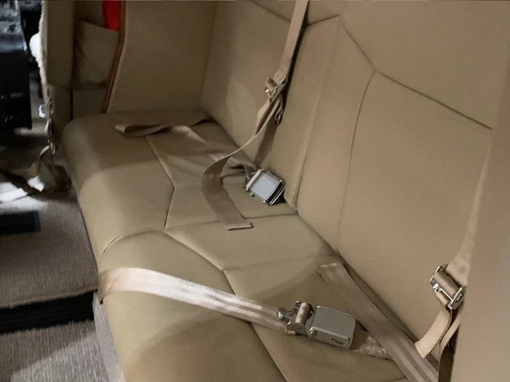 A close-up of a beige leather aircraft seat with a seatbelt.