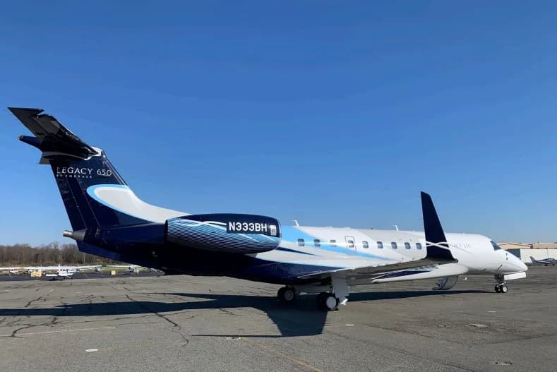 A side view of a white and dark blue Embraer Legacy 650 business jet with registration N333BH parked on an asphalt tarmac.