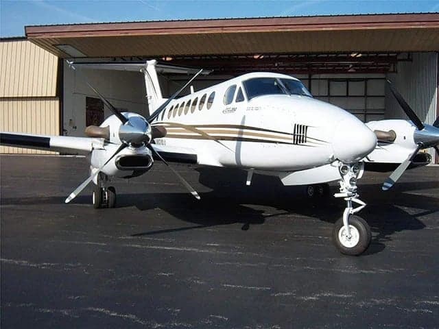 A white Beechcraft King Air with brown and black stripes parked outside an open hangar.
