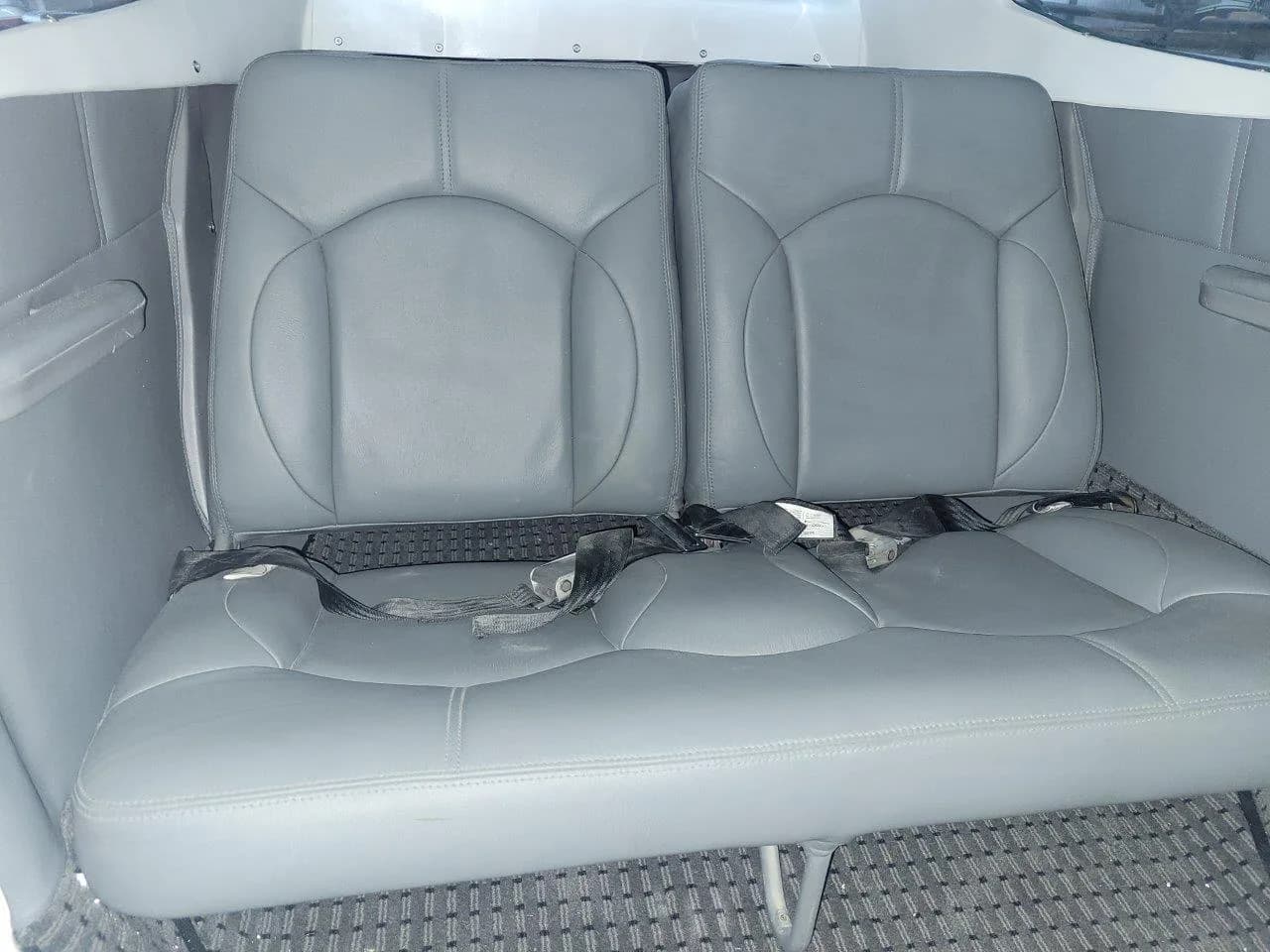 The rear cabin of a small aircraft shows two gray leather seats with seatbelts.