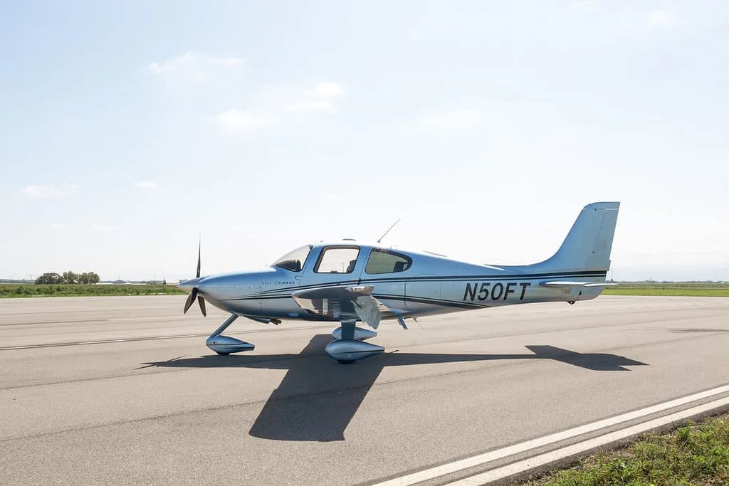 A side view of the light blue Cirrus SR22 aircraft with its doors closed, parked on an airfield.