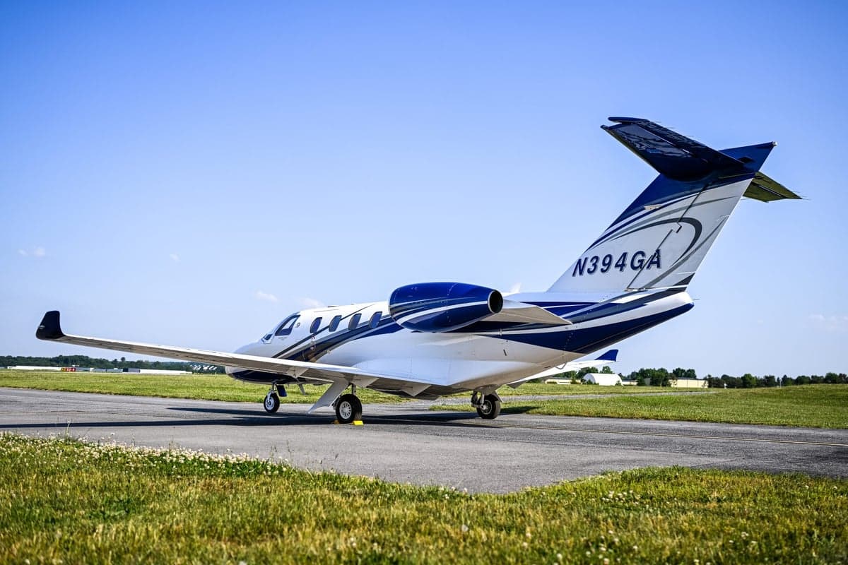 Rear three-quarter view of a white and blue Cessna Citation M2 jet, registration N394GA, on an airport tarmac.